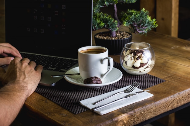 A cup of espresso and tiramisu served for man working in his notebook