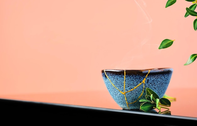 Free photo cup of green japanese tea , tea leaves fly over the cup. selective focus on the cup. steam rises above the bowl. reclaimed ceramic blue cup, second life of things, recycling or kintsugi