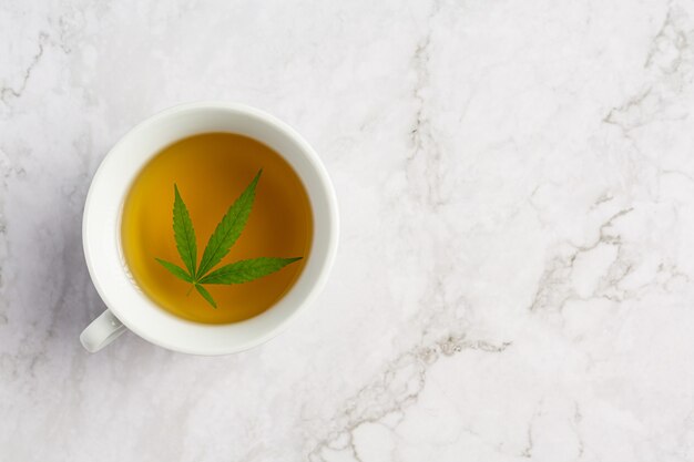 Cup of hemp tea with hemp leaves put on white marble floor