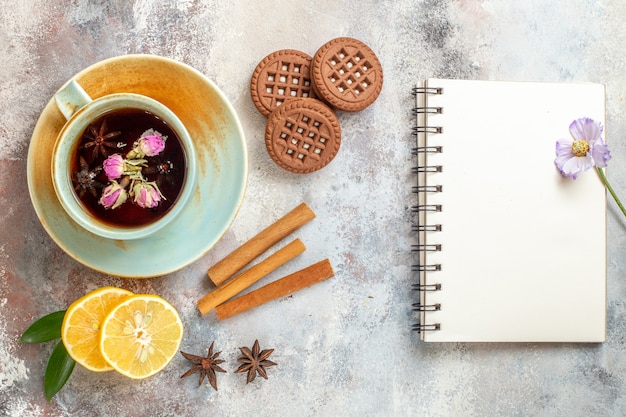 A cup of herbal tea biscuits and cinnamon lime lemon slices and notebook on white table