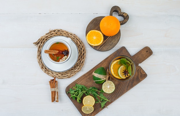 Free photo cup of herbal tea with citrus fruits,mint leaves on cutting boards and cinnamon on white surface