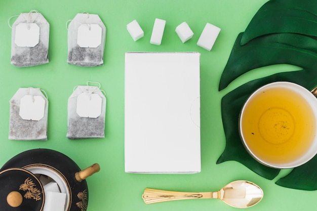 Cup of herbal tea with different types of tea bag and sugar cubes on green background