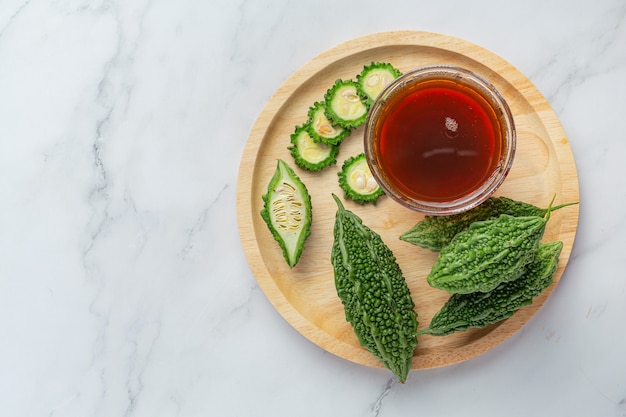 a cup of hot bitter gourd tea with raw sliced bitter gourd on wooden plate