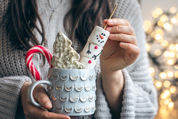 Free photo a cup of hot drink with gingerbread marshmallow and candy in female hands