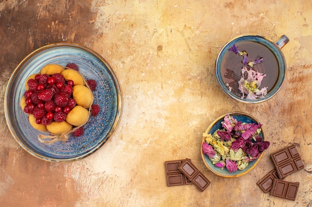 Free Photo a cup of hot herbal tea soft cake with fruits flowers chocolate bars on mixed color table