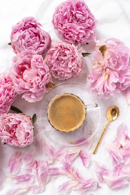 cup of instant coffee on the table with pink peonies under the lights