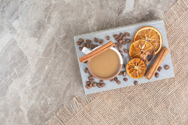 Cup of milk coffee with coffee beans and orange slices on book. High quality photo