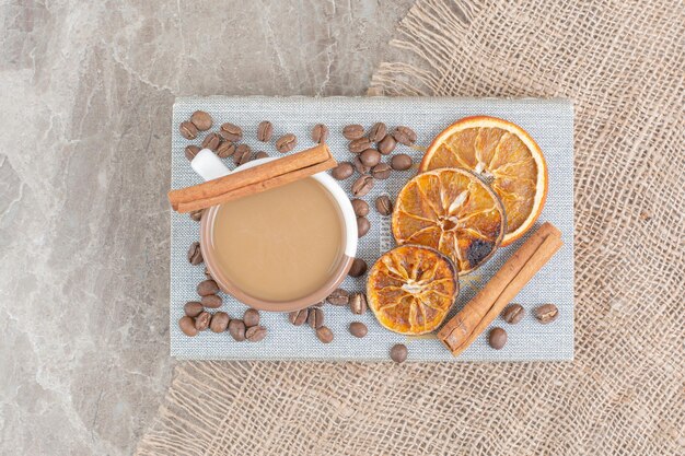 Cup of milk coffee with coffee beans and orange slices on book. High quality photo