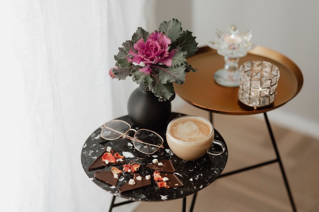 Free Photo cup of milk tea and eyeglasses on a black table next to a curtain