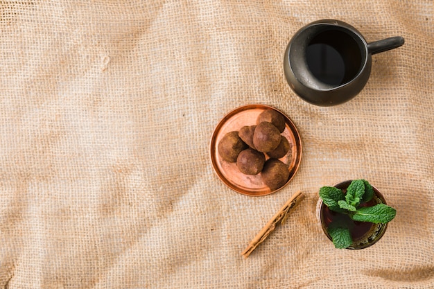 Cup near retro pitcher and sweets on wrinkled burlap