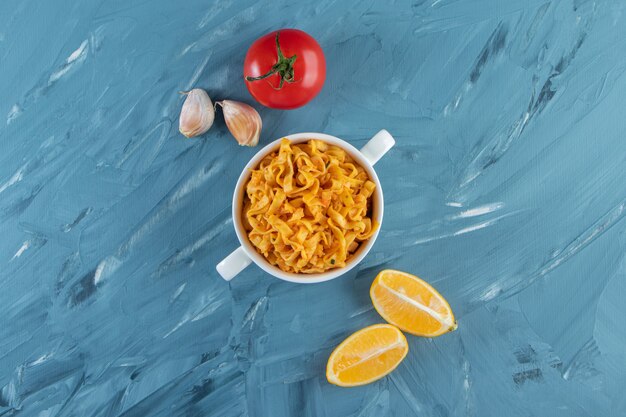 A cup of noodle next to vegetables, on the marble background. 