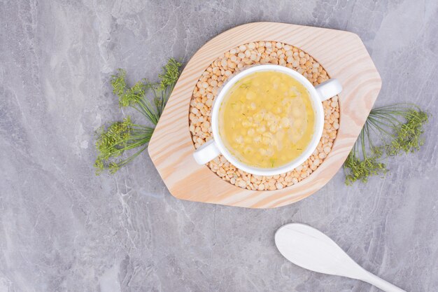 A cup of pea beans soup on uncookes beans in a wooden platter.