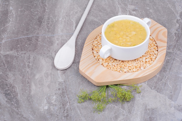 A cup of pea beans soup on uncookes beans in a wooden platter.