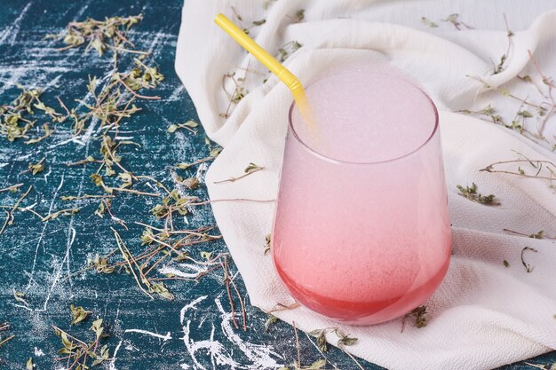 A cup of pink drink with heavy foam on blue.