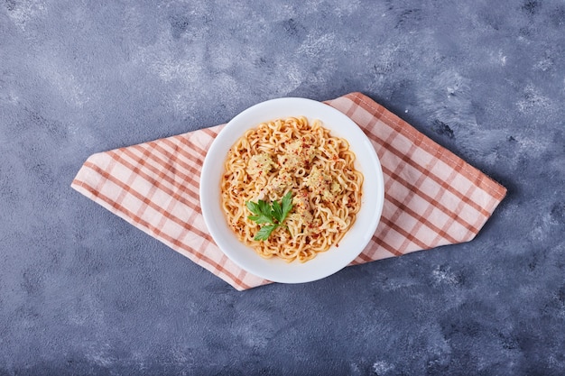 A cup of spaghetti in tomato sauce on kitchen towel.