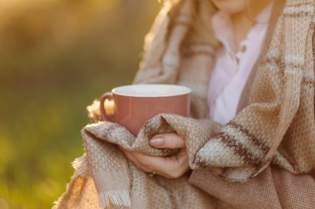 Free photo cup on sunset in hand young girl covered with a blanket