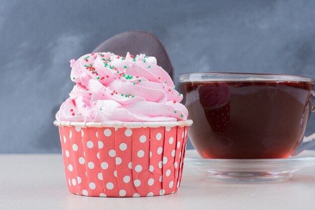 A cup of tea and cupcake on white table.