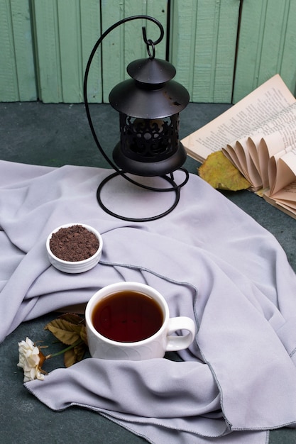 Free photo a cup of tea and herbs in a saucer on the table, a book around