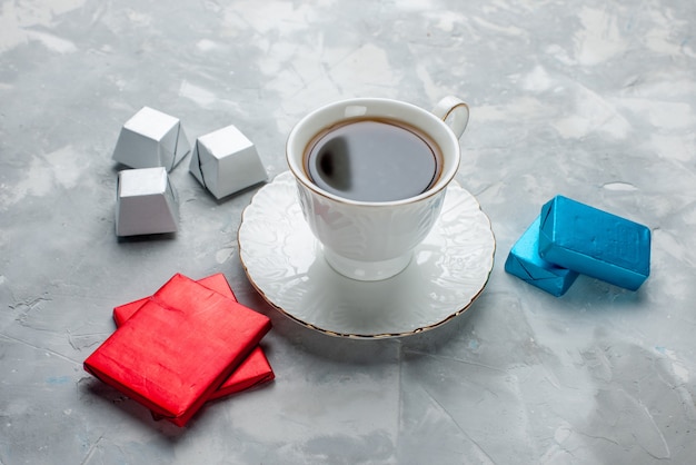 cup of tea hot inside white cup on glass plate with silver anded package chocolate candies on light desk, tea drink sweet cookie teatime