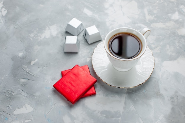 cup of tea hot inside white cup on glass plate with silver package chocolate candies on light desk, tea drink sweet chocolate cookie