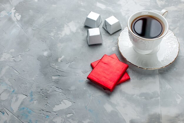 cup of tea hot inside white cup on glass plate with silver package chocolate candies on light desk, tea sweet chocolate cookie