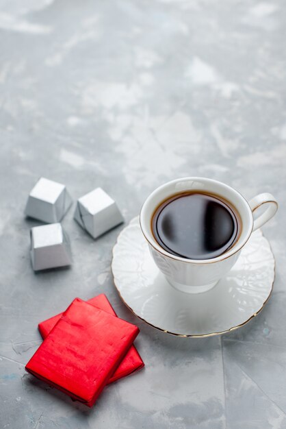 cup of tea hot inside white cup on glass plate with silver package chocolate candies on light floor tea drink sweet chocolate teatime