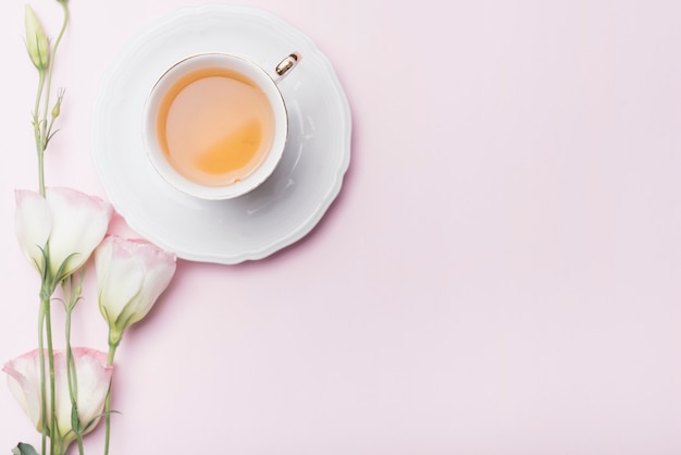 Cup of tea with eustoma flowers on pink background