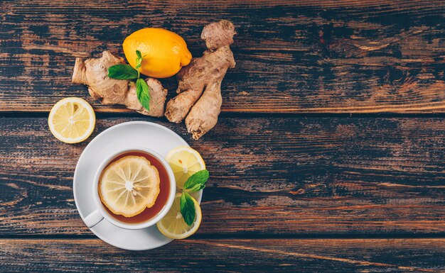 A cup of tea with ginger, lemon flat lay on a dark wooden background space for text