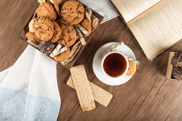 A cup of tea with oatmeal cookies and crackers on a wooden table