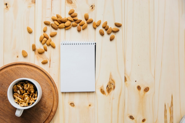 Free Photo cup of walnut near blank notepad and almonds on wooden backdrop