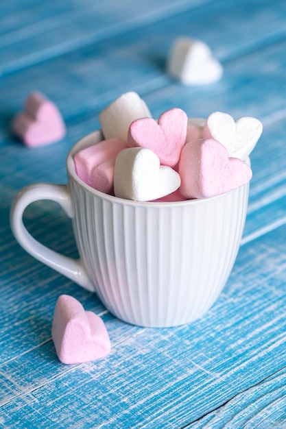 A cup with heartshaped marshmallows closeup on a blue wooden background