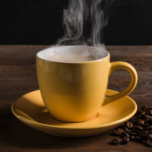 Cup with hot beverage near coffee beans