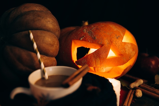 Free Photo cup with hot chocolate stands before shiny scarry halloween pumpkin