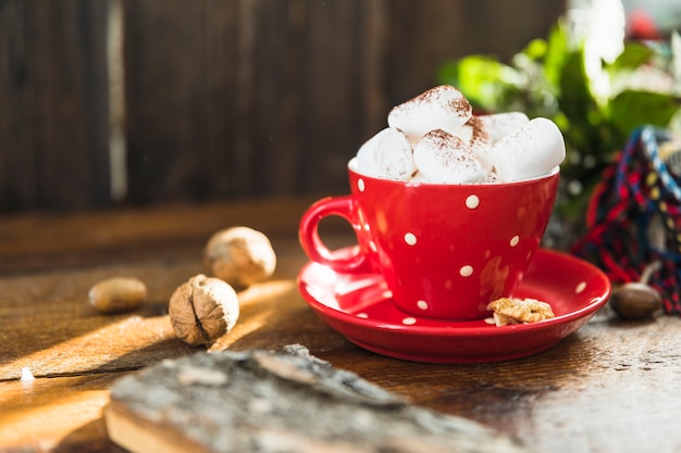 Cup with marshmallow on plate near walnuts