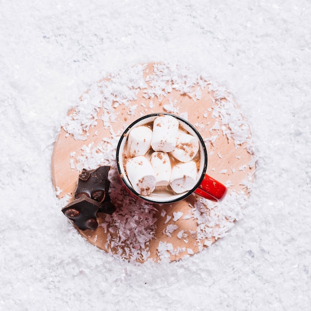 Free photo cup with marshmallows near chocolate on stand between snow