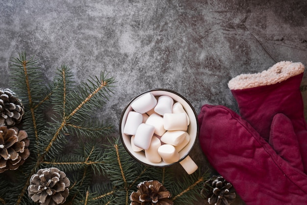 Cup with marshmallows near fir twigs and mittens 