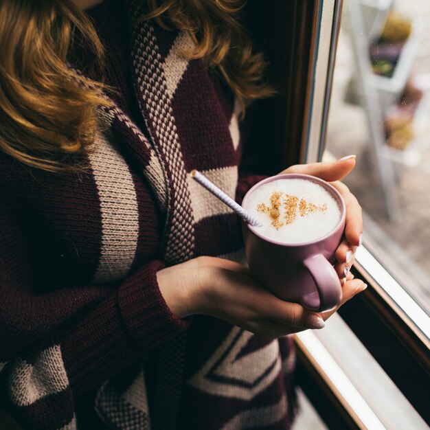 Cup with milk foam and Christmas tree of cinnamon held in woman's arms