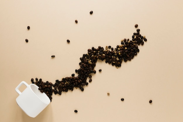 Free photo cup with spilled coffee beans on beige table