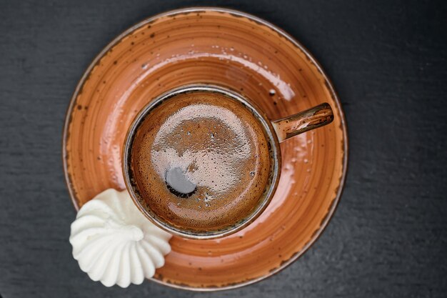 A cup with strong Turkish coffee on a black old table next to the bizet top view