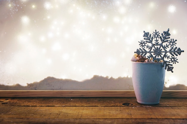 Free photo cup with toy snowflake on wood table near bank of snow and fairy lights