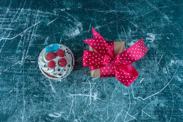 A cupcake and a small gift box on blue background. High quality photo