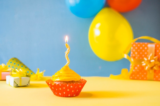 Free photo cupcake with burning candle on yellow surface