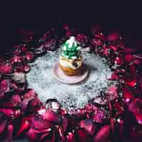 Free photo cupcake with glaze fir tree on top stands in the circle of rose petals