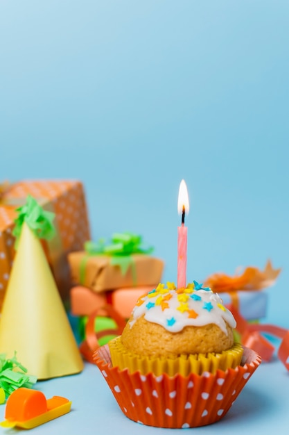 Cupcake with lit candle and birthday arrangement behind it