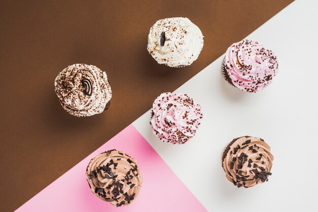 Cupcakes with different frosting on multicolored backdrop