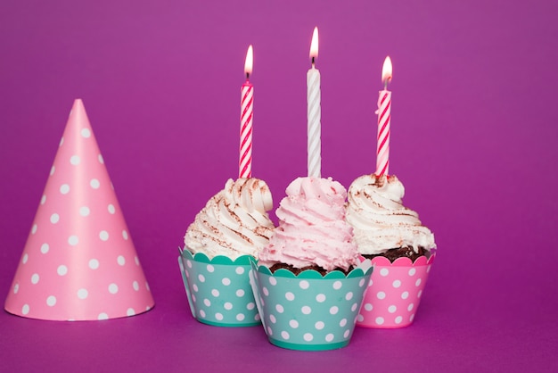 Free photo cupcakes with lit candle next to hat