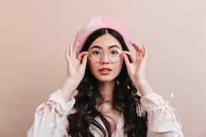 Free photo curious chinese woman posing in glasses. fashionable asian woman in beret isolated on beige background.