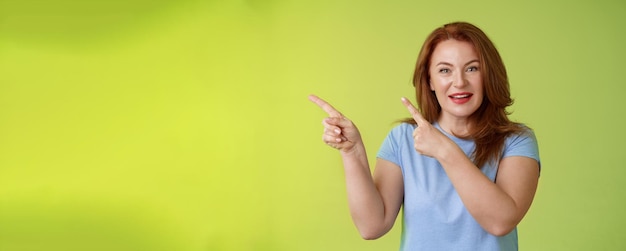 Free Photo curious enthusiastic gorgeous redhead female intrigued pointing upper left corner asking question interesting product talk shop assistant consulting promo stand green background blue tshirt