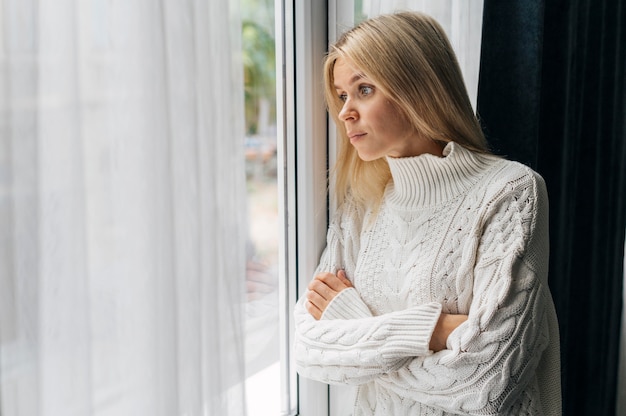 Free photo curious woman at home during the pandemic looking through the window