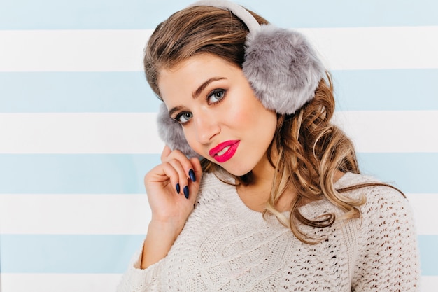 Free photo curly brown-haired woman in white knitted sweater looks cute and shy, posing for close-up portrait